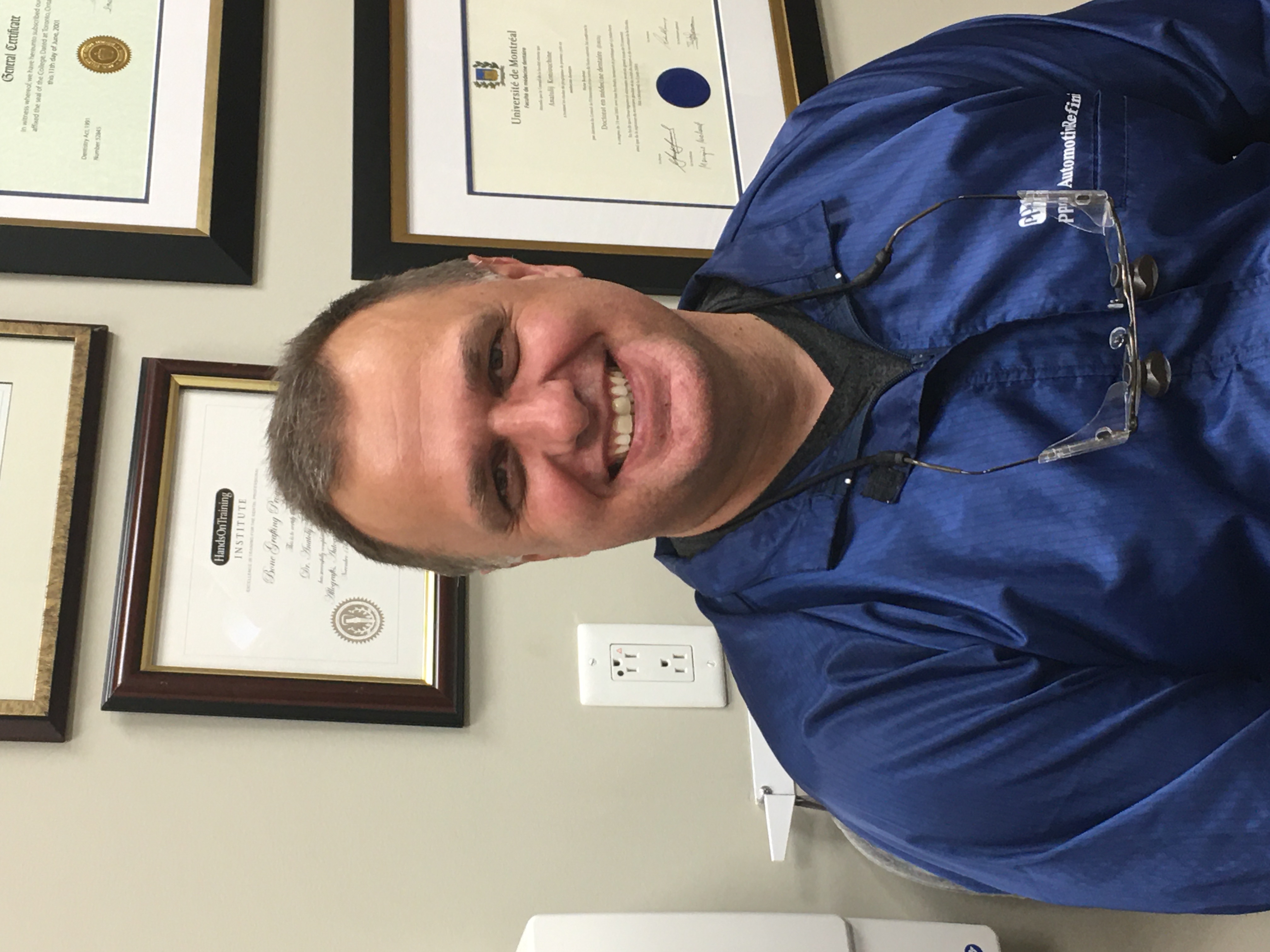 Dr. Anatolij Koniouchine smiling in front of his credentials wall at Dental Sedation Ottawa